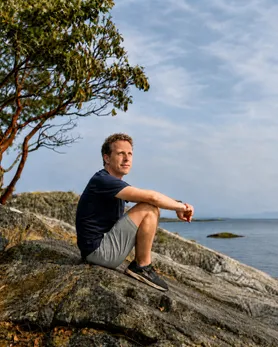 Dan Buhler, sitting on a granite shore under an arbutus, looking out over the water.